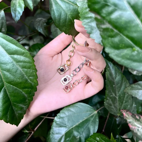Girl holding a variety of camera photo keychains, showcasing platinum, gold, rose gold, and black options.