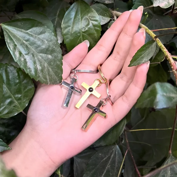 Woman holding silver, gold, and rose gold Bible verse cross keychains in her palm, symbolizing faith and unity.