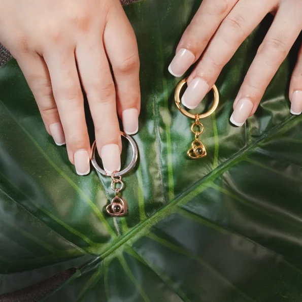 A woman holding gold and silver heart photo keychains, capturing unforgettable moments forever.